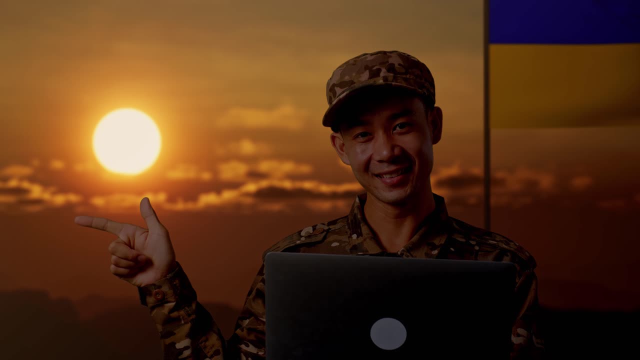 Soldato sorridente con portatile al tramonto, sfondo con bandiera ucraina