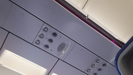 the overhead panel of an airplane cabin, featuring air vents, lighting controls, and possibly an announcement speaker system, capturing a common sight for travelers