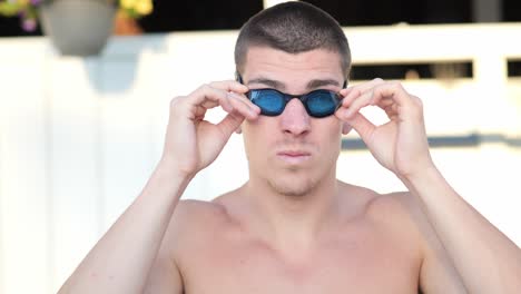 Young-attractive-swimmer-puts-on-his-swimming-goggles-frontal-close-up
