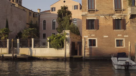 Brick-Facade-with-balcony-of-building-in-Canal-Grande-and-boats-at-the-small-pier,-Morning,-Venice,-Italy