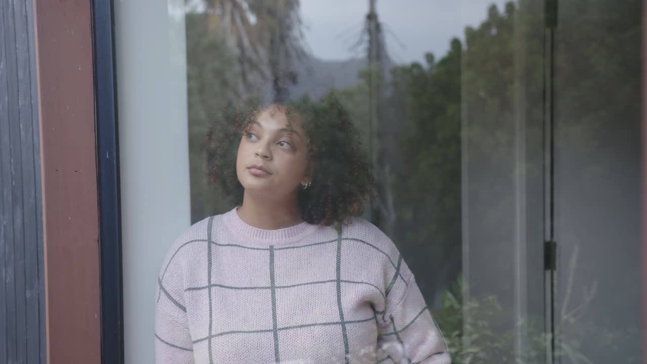 Standing by window, plus size woman in casual sweater looking outside thoughtfully