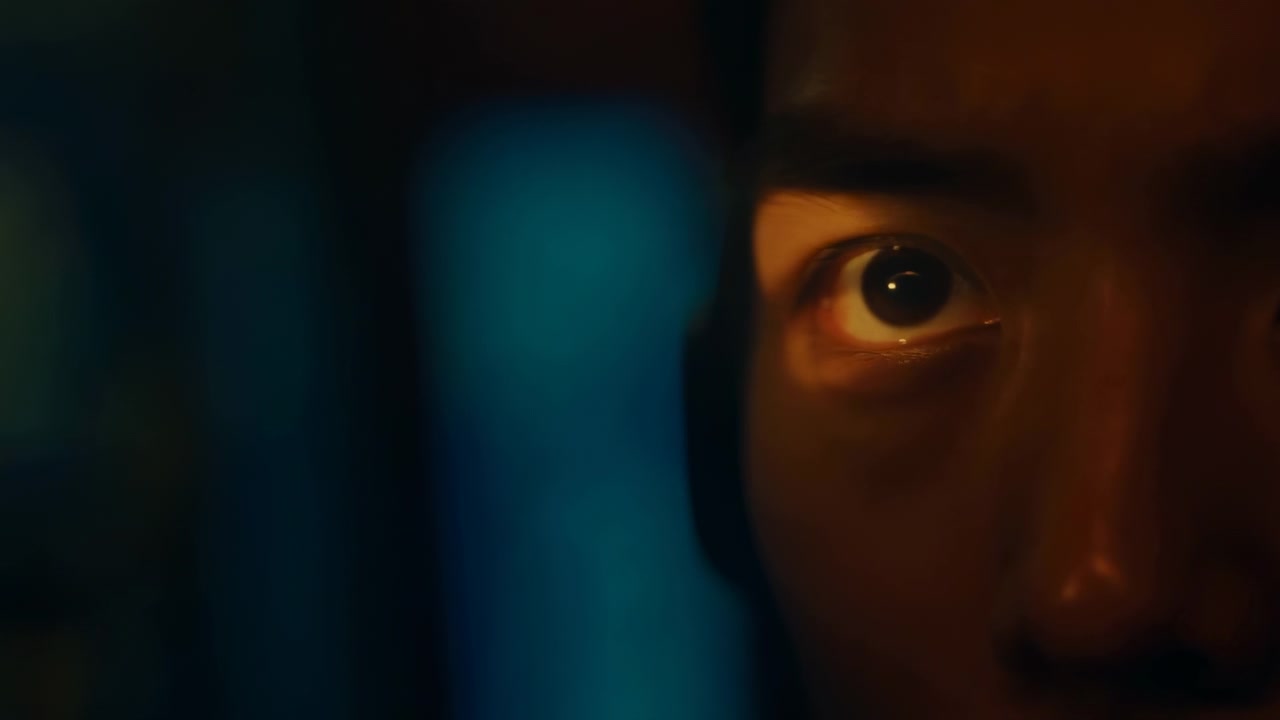 Single human eye and upper face shown in extreme closeup as bright amber light sweeps across intense gaze, revealing glossy reflection, tense focus, dark texture and dramatic contrast