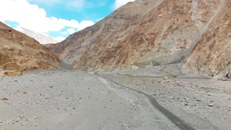Small road crossing thought a big empty rocky area with majestic mountains in Shyok, ladakh, India