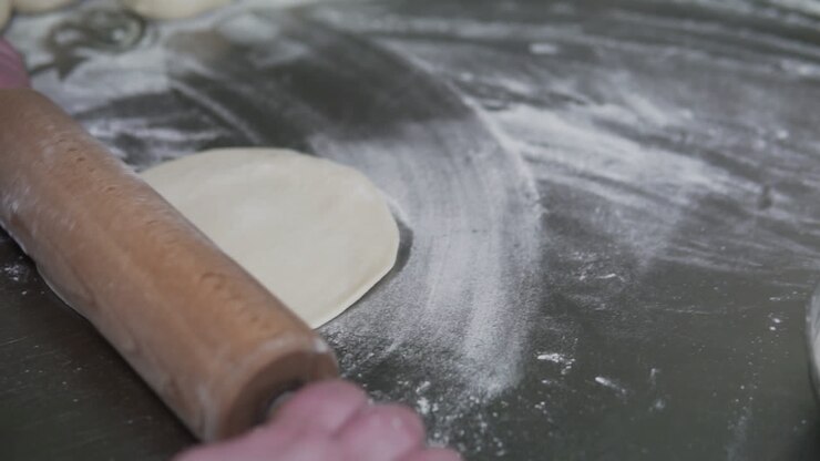 Close-up view of hands rolling dough with a wooden rolling pin