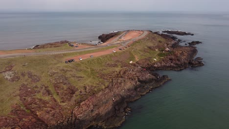 Aerial-view-of-cars-driving-on-top-of-cliff,-watching-ocean-view-during-cloudy-day-in-Punta-Ballena-Area