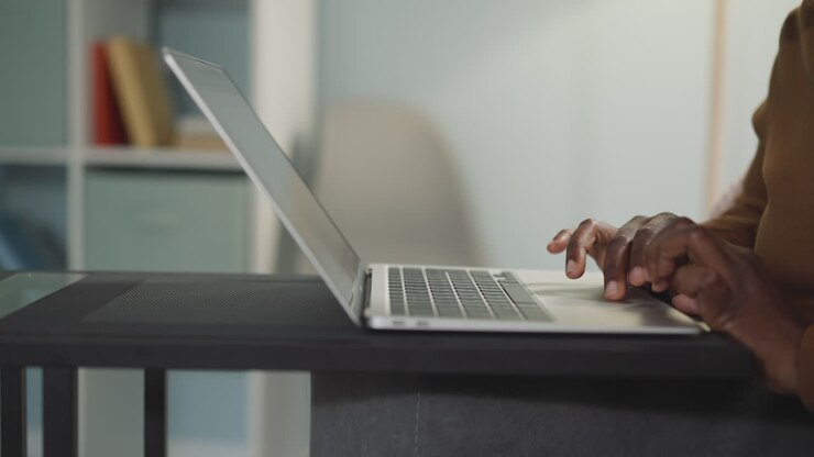 Afroamerikanische Frau sitzt am Tisch und arbeitet am Laptop.