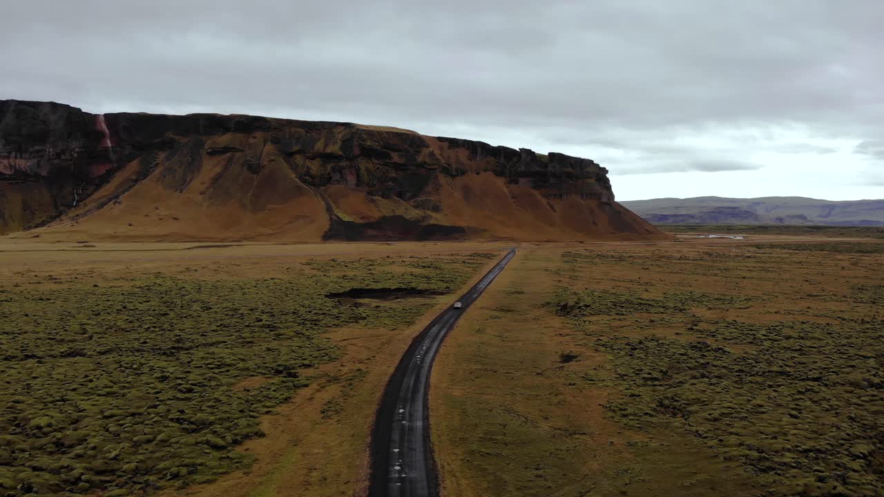 vista aérea en 4k de un automóvil conduciendo en una carretera sucia rodeada de un campo de lava de musgo verde con un hermoso paisaje montañoso, islandia, europa, disparo de trípode de avión no tripulado
