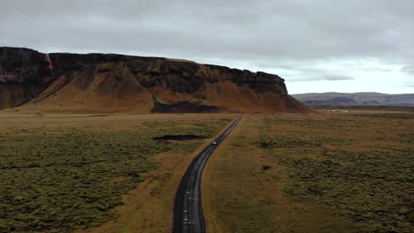 Vista-Aérea-4k-De-Un-Automóvil-Conduciendo-Por-Una-Carretera-Sucia-Rodeada-De-Un-Campo-De-Lava-De-Musgo-Verde-Con-Un-Hermoso-Paisaje-Montañoso,-Islandia,-Europa,-Disparo-De-Trípode-De-Drones