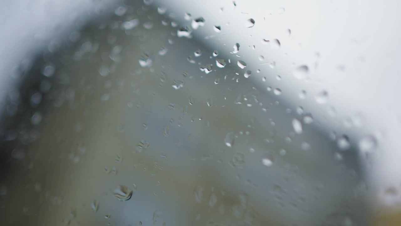 Raindrops on car window, blurred cityscape outside, rainy urban drive