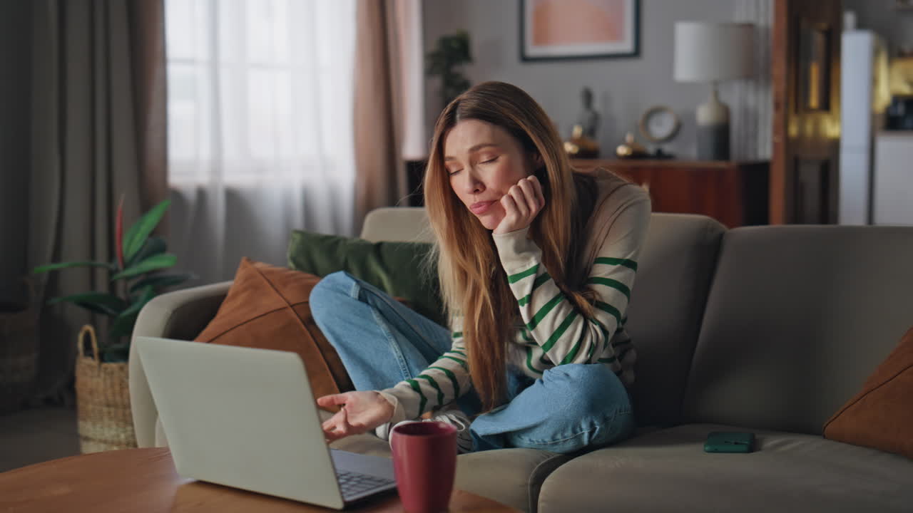 Ragazza in videochiamata al laptop in salotto. Donna sorridente che parla in una riunione online.