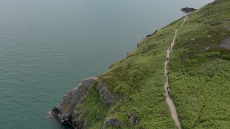 drone flying and people walking on a small path in a large mountain near the sea on a sunny day