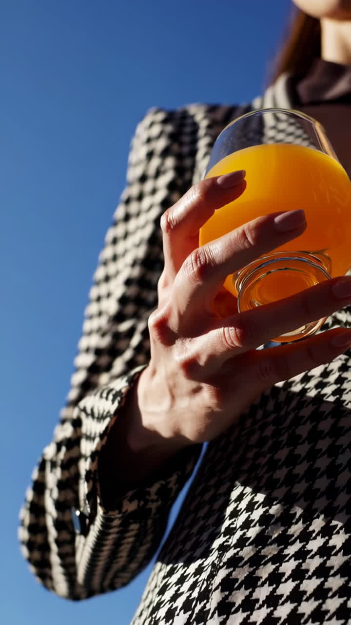 Person Holding a Glass of Orange Juice Against a Blue Sky