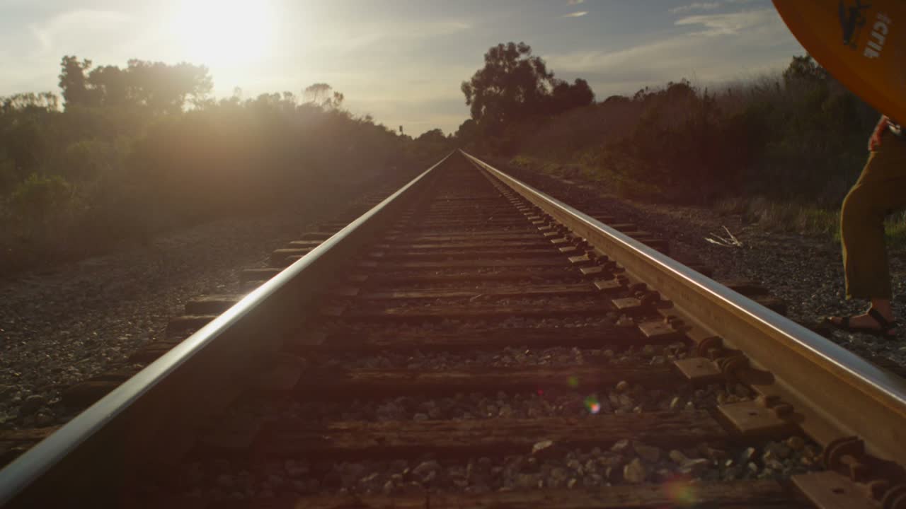 한 서퍼가 해안 지역의 외딴 서핑 장소로 하이킹을 하면서 기차 선로 위로 보드를 옮깁니다.