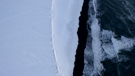 AERIAL:-View-over-Black-Beach-with-white-arctic-snow-Mountains,--Landscape-in-Iceland-in-Winter-Snow,-Ice,-Waves,-Water