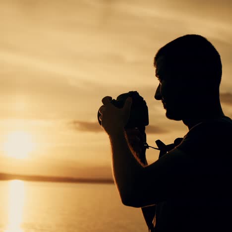 a man looks at the photos in the camera near the river at sunset. the guy chooses the best photos