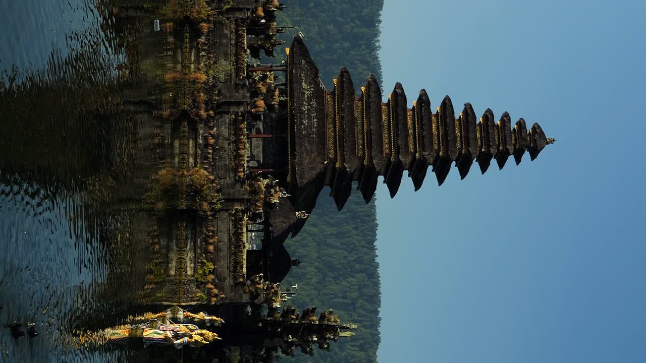 Vertical slow motion panning shot of Pura Ulun Danu temple with view of volcanic lake and surrounding nature with swimming ducks
