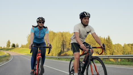 Steadicam-shot-of-mountain-biking-couple-riding-on-bike-trail-at-sunset-doing-high.