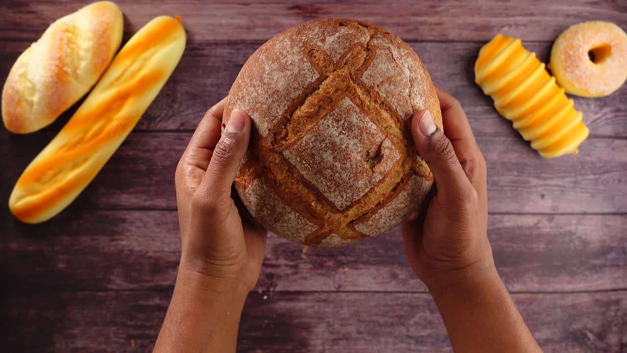 Hands Holding and Rotating a Fresh Loaf of Sourdough Bread