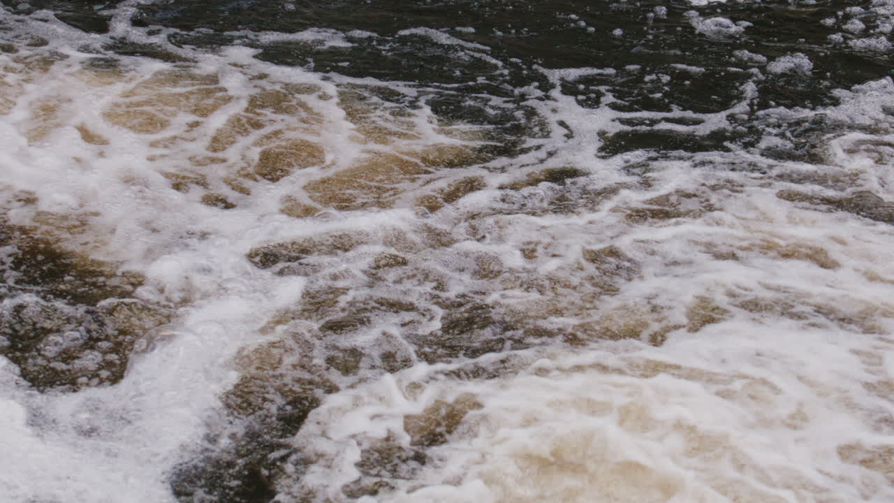 Close-up of swirling river foam and bubbling surface in slow-motion, evoking flow, turbulence, and calmness.