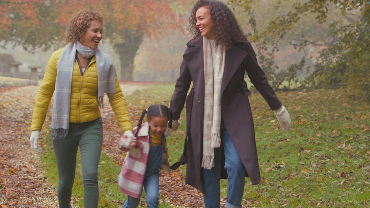 Famiglia femminile multigenerazionale sorridente che cammina nella campagna autunnale, facendo dondolare la nipotina in aria