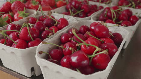 cerezas rojas en cajas pequeñas para la venta en una tienda de la granja, fresas en el fondo, paralaje de mano