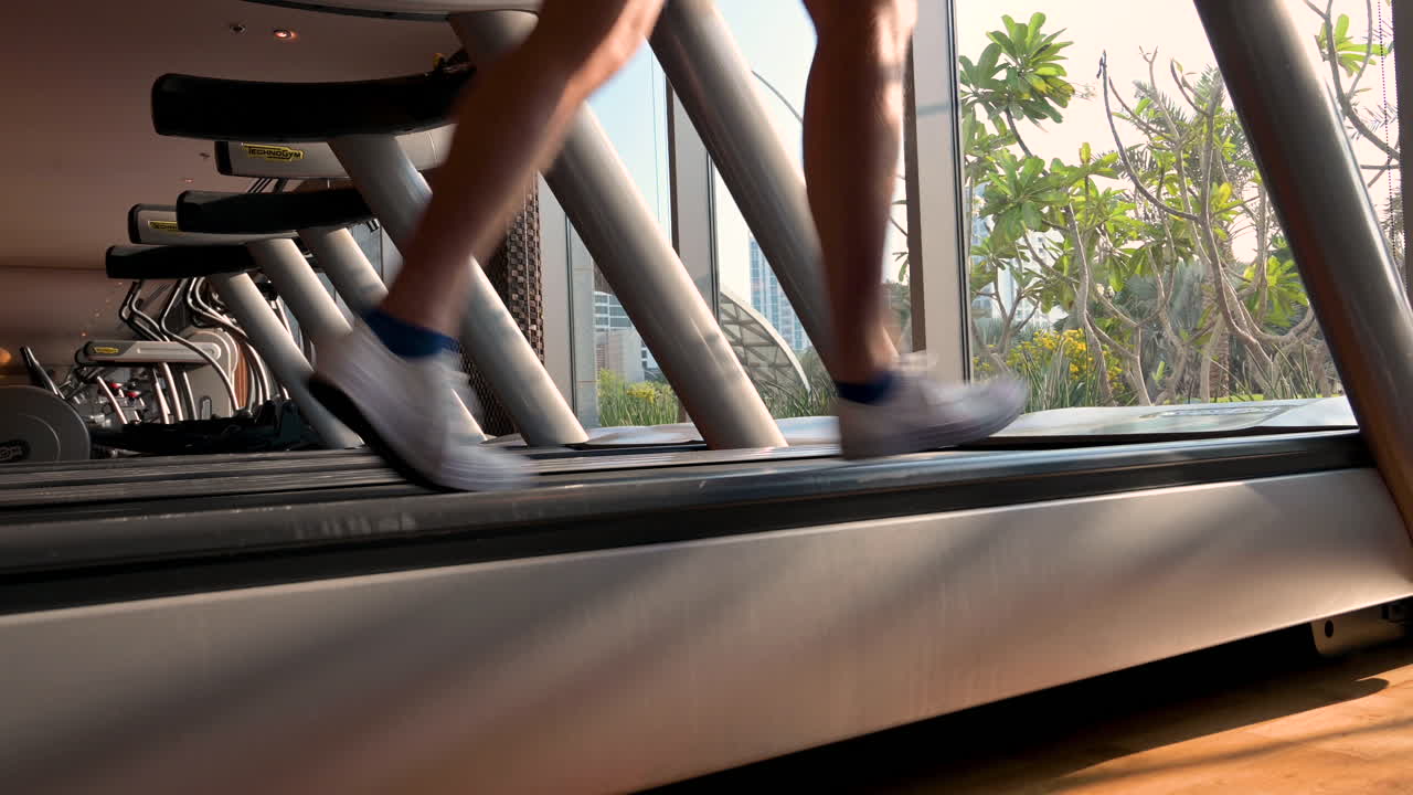 Sporty man legs running on running machine in the gym fitness room with window glass and garden background