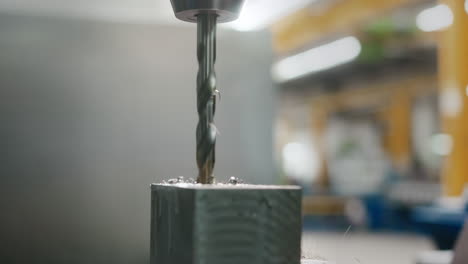 a drill bit working on a block of metal in a big factory