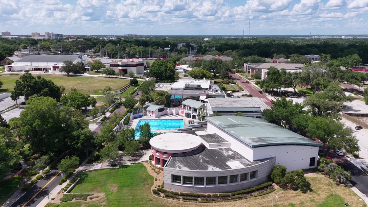 Edificio curvo di Frank Lloyd Wright che si affaccia sul lago, rimessa per barche in legno sul molo, strada alberata, nuvole sparse, campus del Florida Southern College, Lakeland, Florida, USA. Ampia ripresa aerea con drone