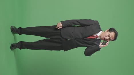 full body of angry asian business man talking on mobile phone while standing on green screen in the studio