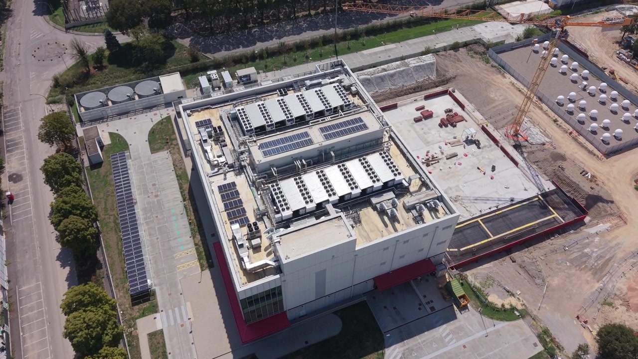 Luftfoto af datacenteranlæg med industribygninger, køleenheder, solpaneler og byggepladser i Milano, Italien