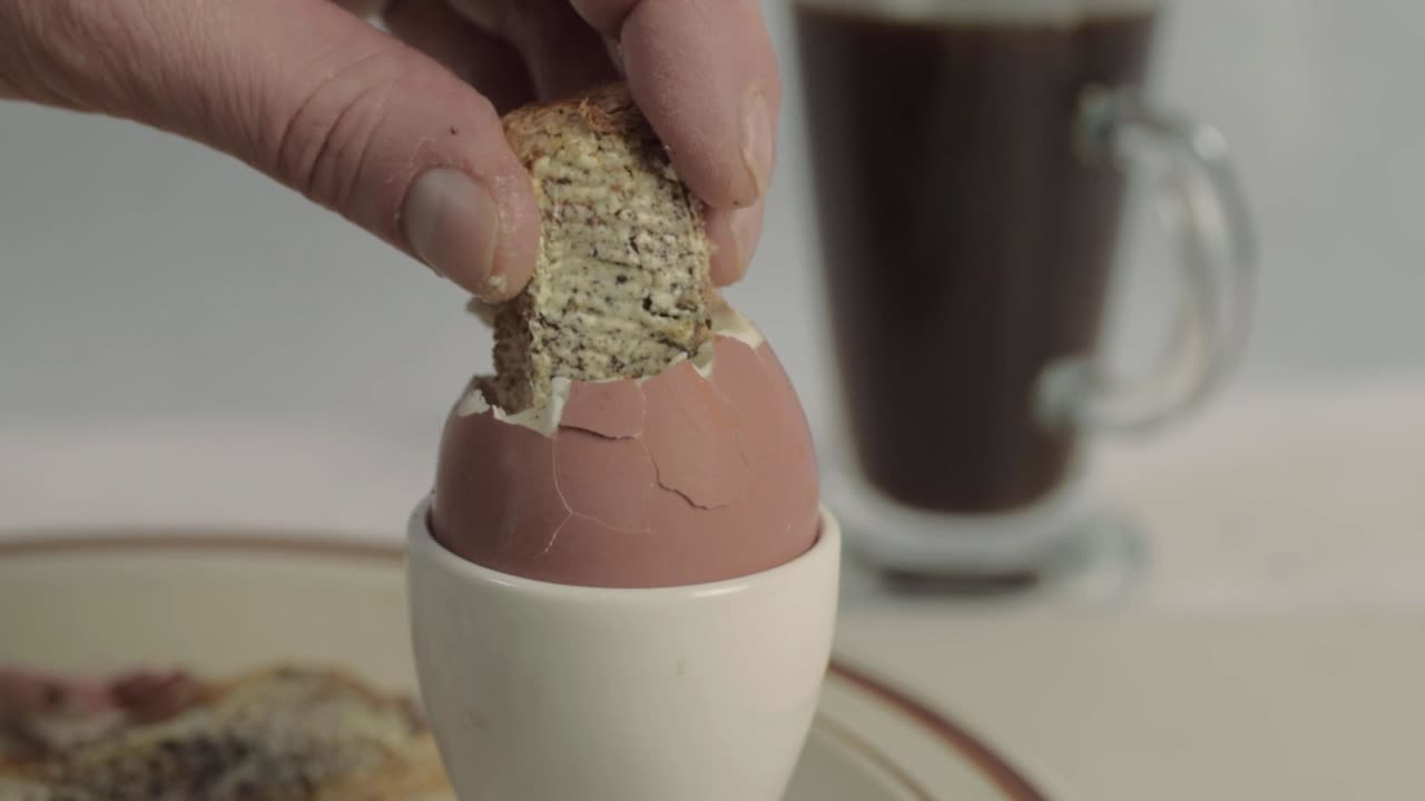 Hand dipping toasted bread soldiers into a boiled egg