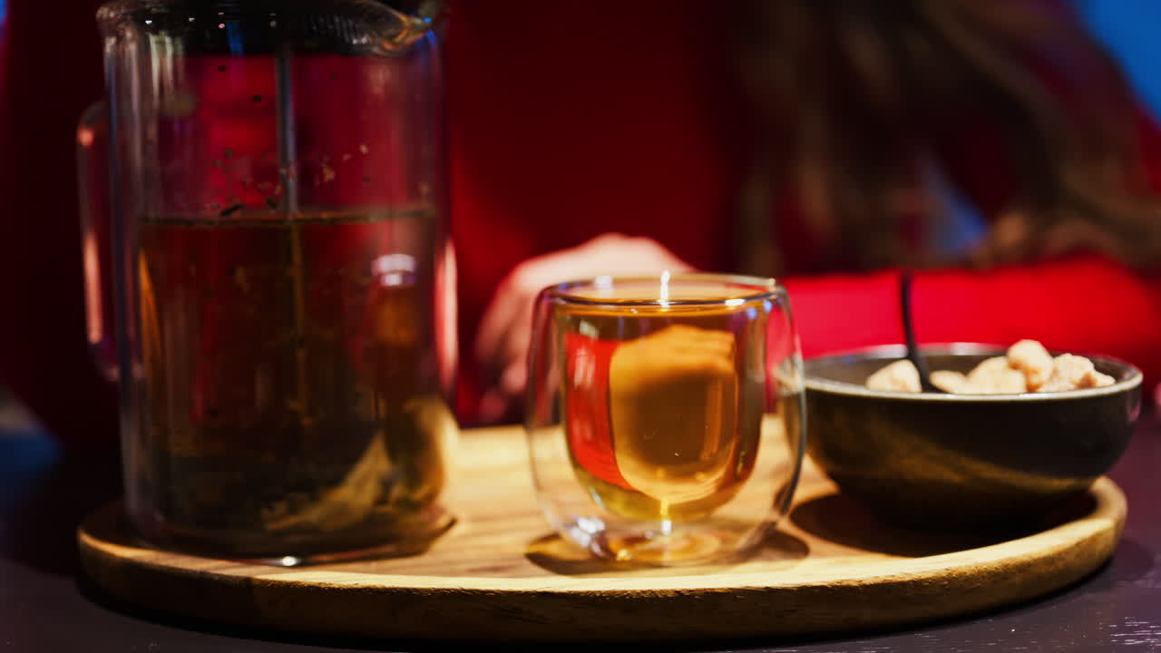 Close up of a woman pressing down the tea leaves with the help of a French press near a cup of tea at a restaurant
