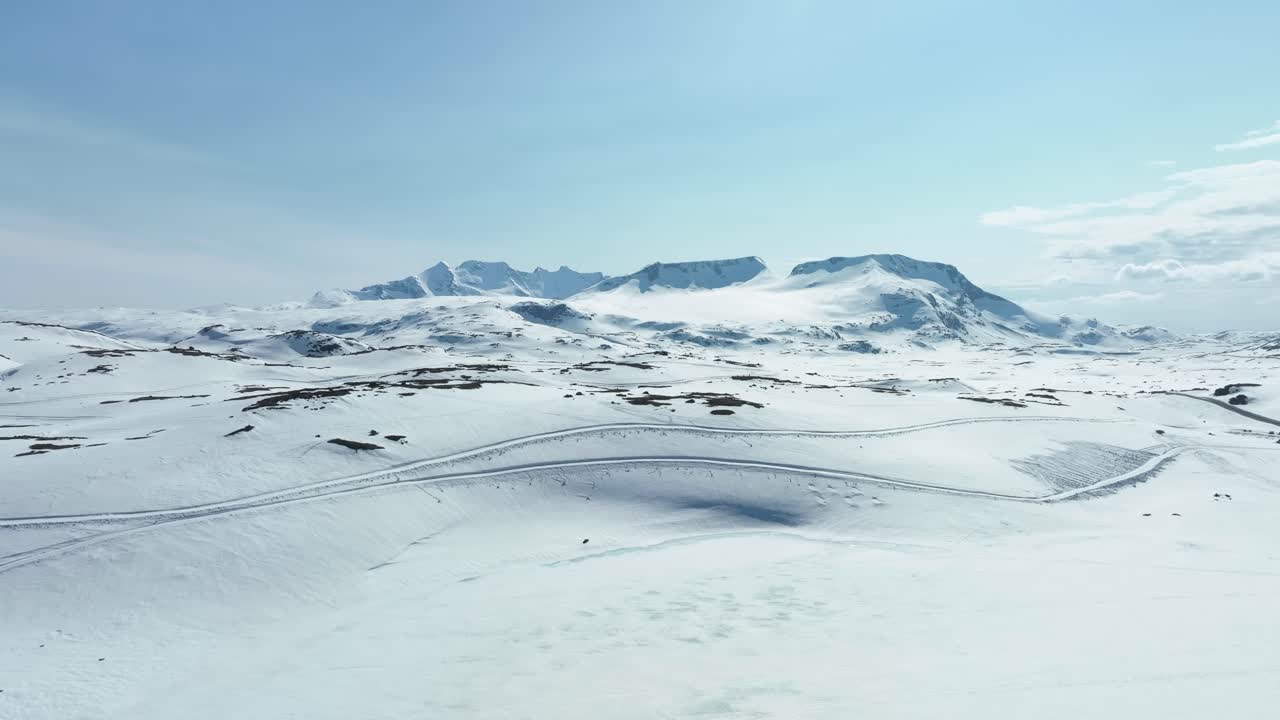 Hurrungane- og Jotunheimen-bjergene set fra toppen af vejen over Sognefjellet i Norge – Snescooterspor krydser sneen i forgrunden.