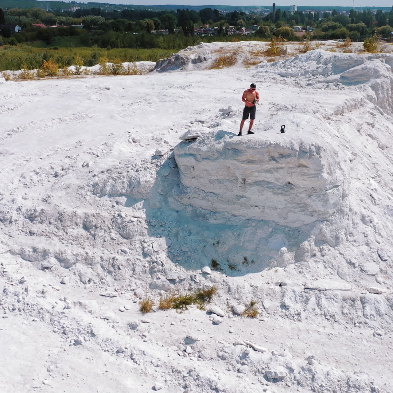 Sportsman drinks water on a white canyon. Strong man standing on the edge of a hill near the city. Aerial view. Camera moves round.