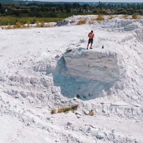 sportsman drinks water on a white canyon. strong man standing on the edge of a hill near the city. aerial view. camera moves round.