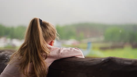 adorable girl leans on log handrail and watches helicopter