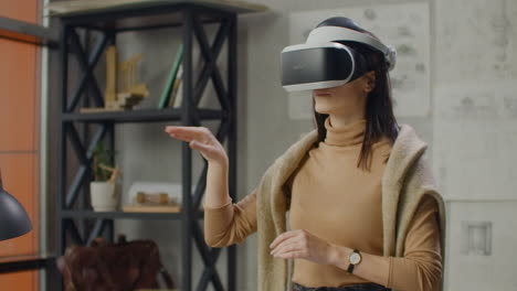 young woman designer in office in virtual reality helmet with hands makes movements imitating the work of graphic interface.