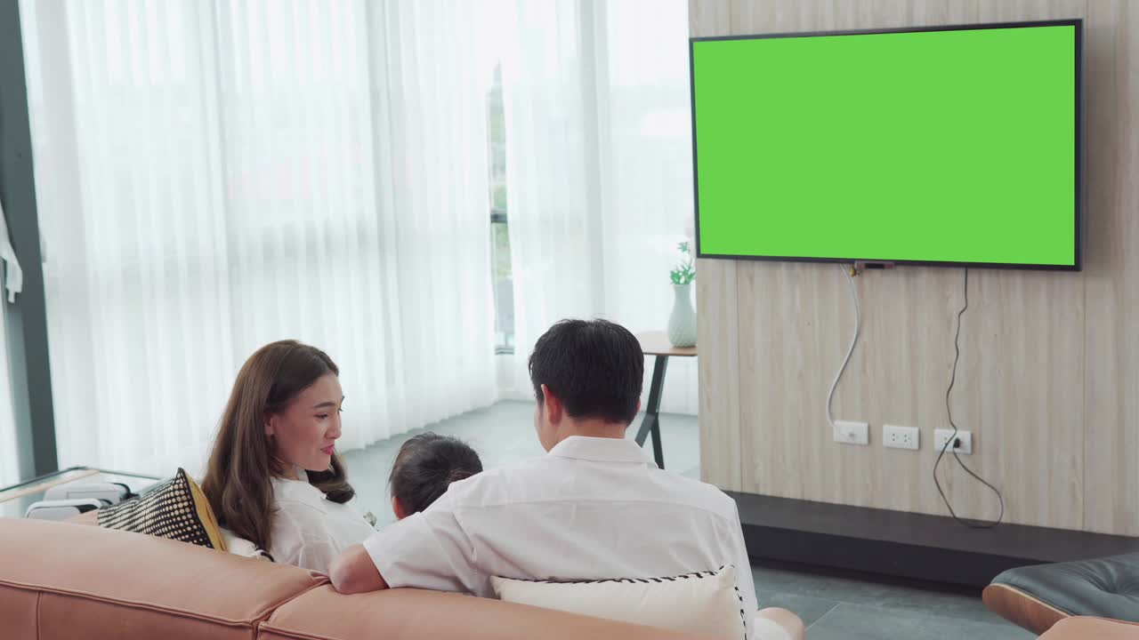 행복한 아시아 가족은 집에서 거실에서 텔레비전을 보고 함께 리티 타임을 보내고, 메시지를 위해 녹색 스크린 모니터로 채널을 전환합니다.