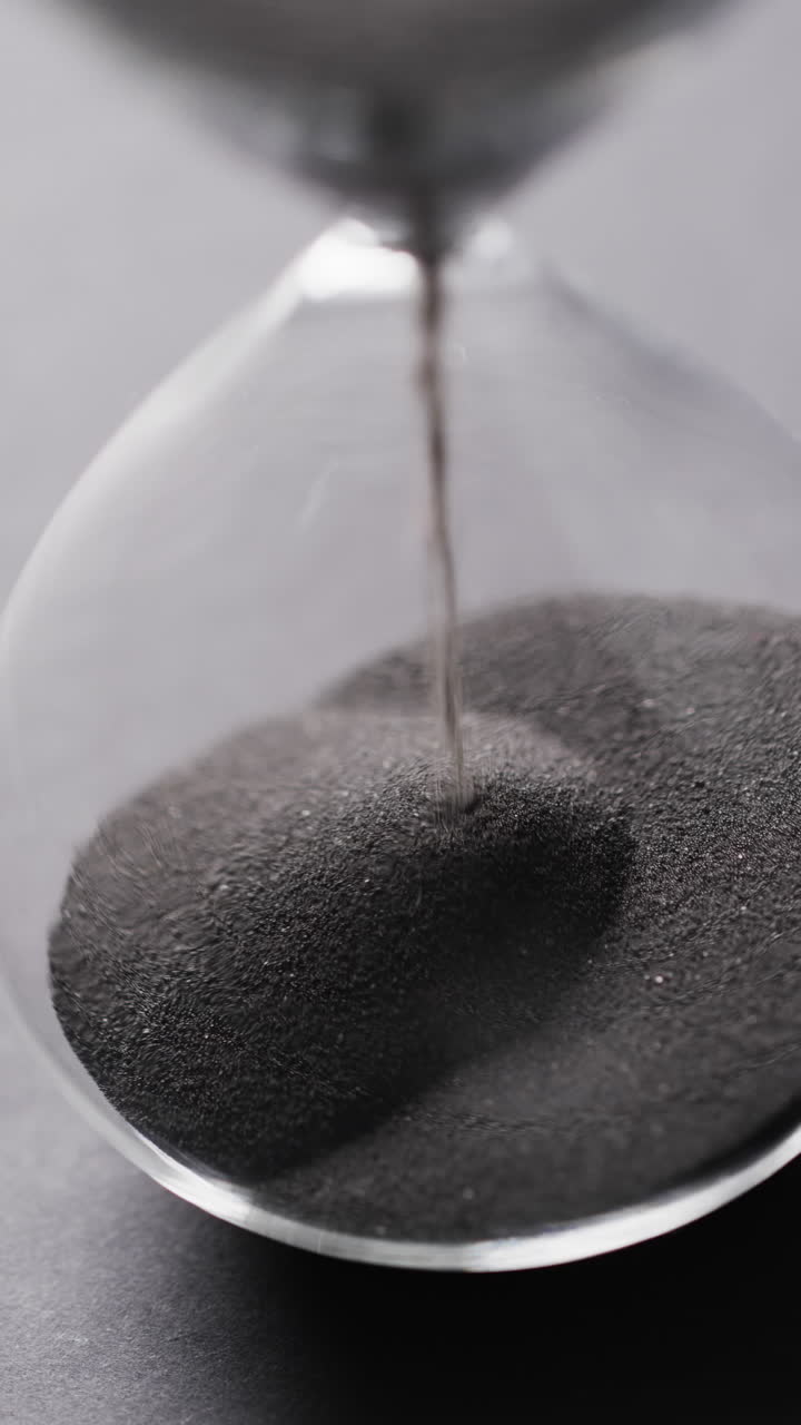 Vertical video of hourglass with sand pouring, copy space on grey background