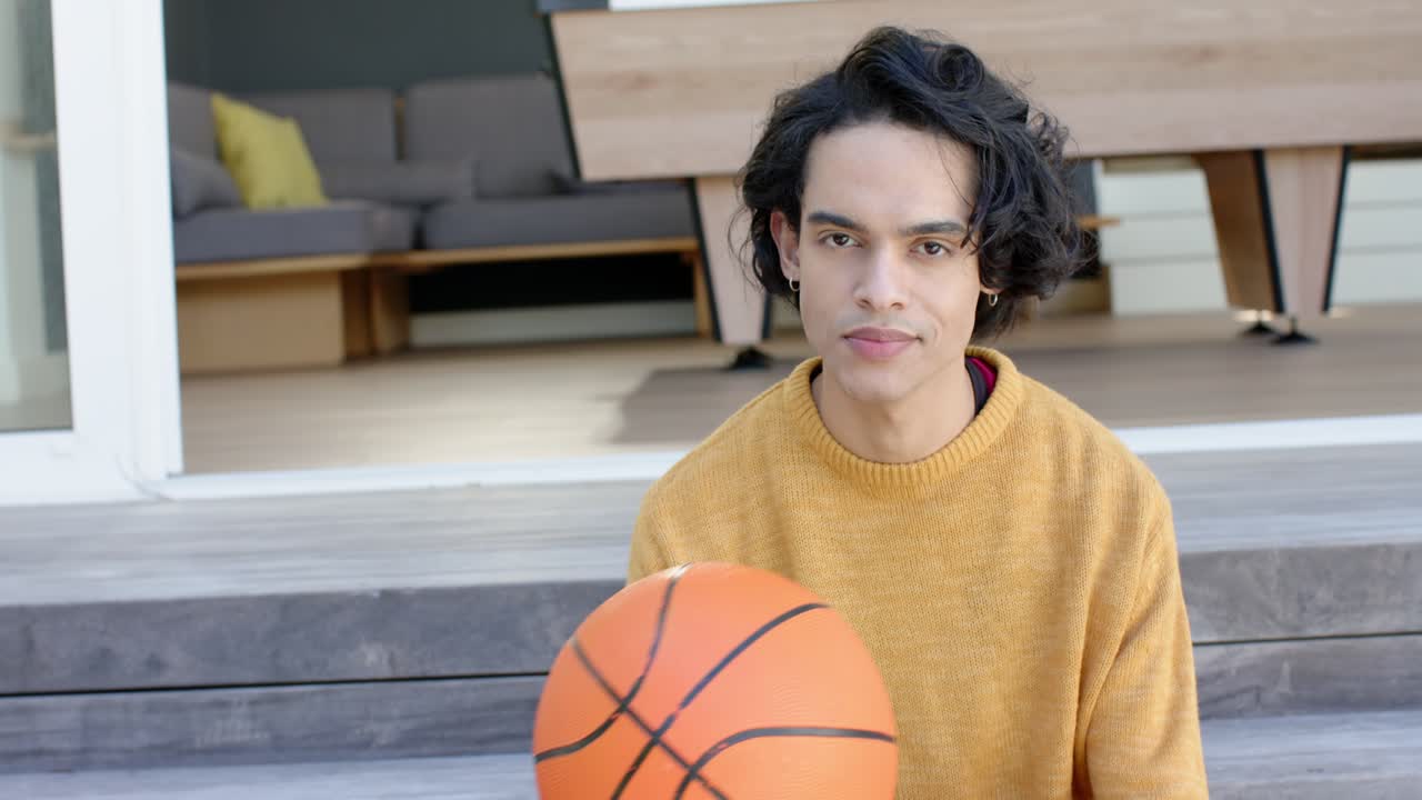 Uomo sui vent'anni che palleggia con un pallone da basket su una piattaforma di legno, si ferma tenendolo in grembo e riprende a palleggiare