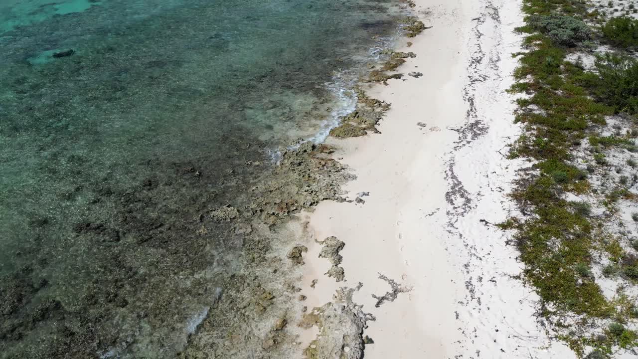 las imágenes de drones se inclinan lentamente para revelar las olas rompiendo un arrecife de coral en un hermoso océano tropical con huellas en la arena en la playa de las islas caimán en el caribe