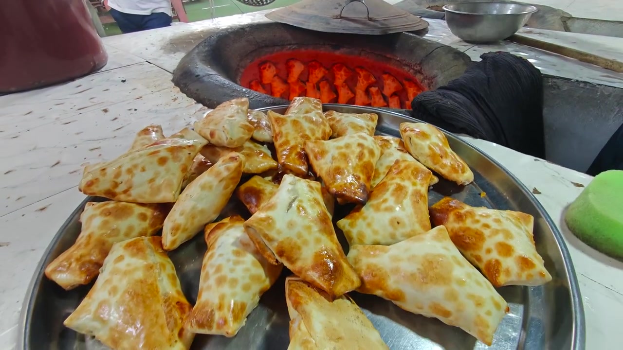 Fornaio che rimuove samsa appena sfornati da un tradizionale forno tandoor