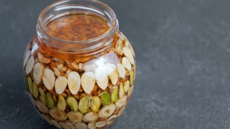open jar with nuts in honey on black table close-up.