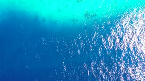 copy space with blue turquoise sea texture of surface reflecting sunshine, rocks and white sand of bottom seen through clear water in coastline of cook islands