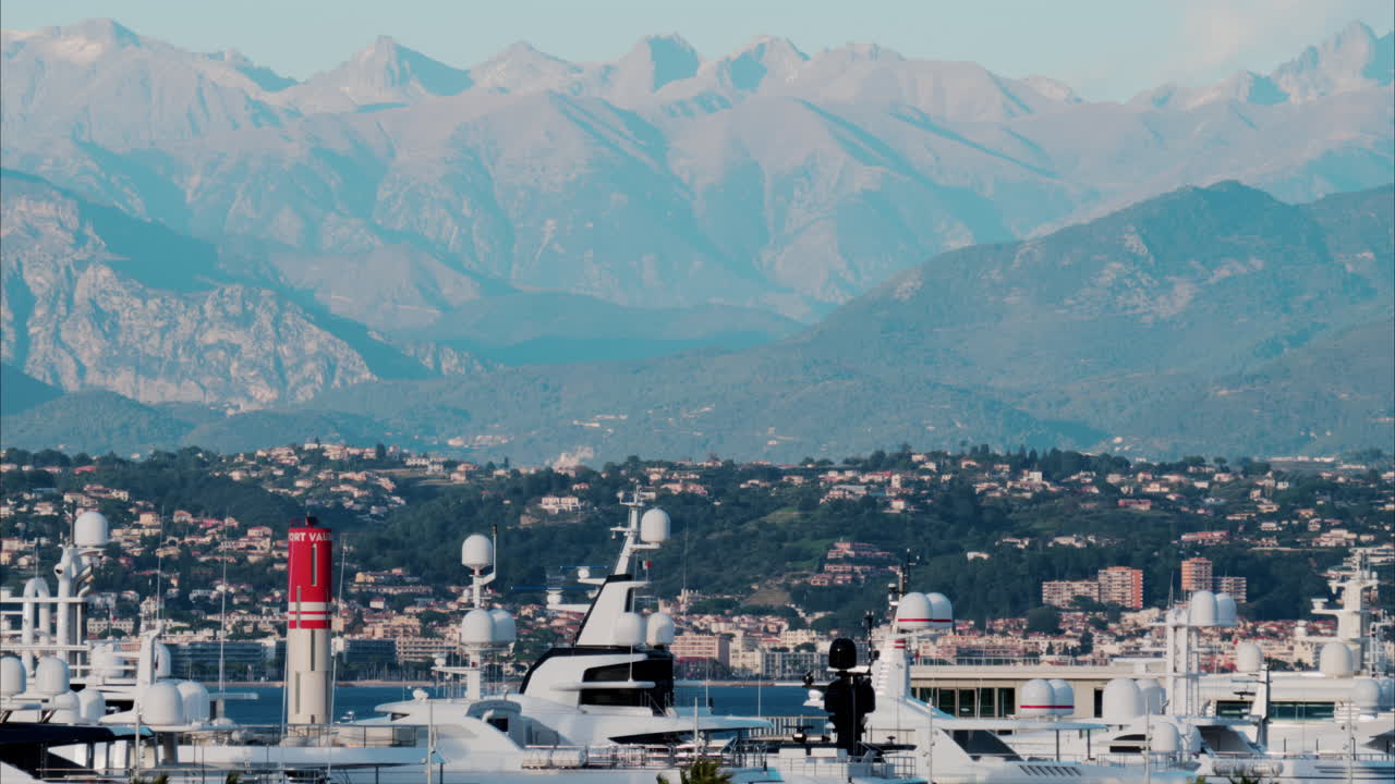 Multiple boats docked in the Port Vauban in Antibes, France with a view of the mountains in the background