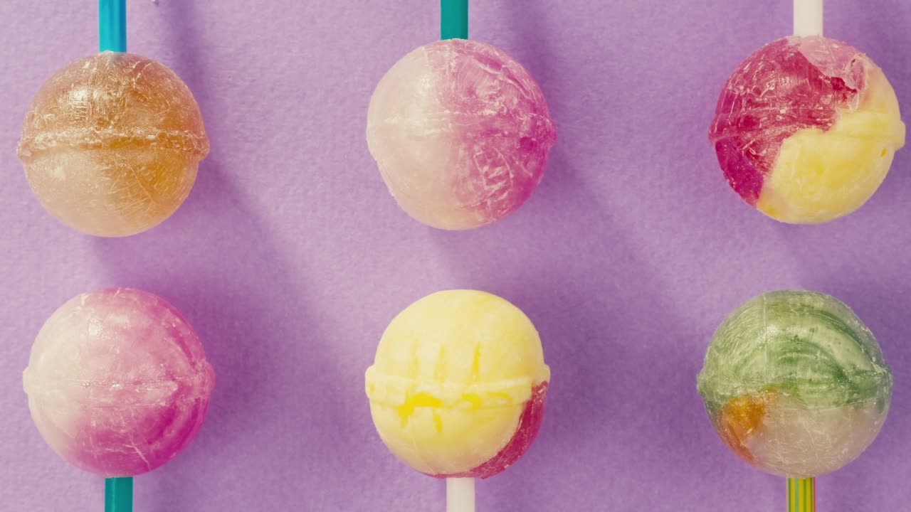 Sweet lollipops with glitter sprinkles on color purple background zoom frame. Bright texture sugar candies close up top view. Composition of favorite children's summer sweets. Studio shot for shop, supermarket, confectionery