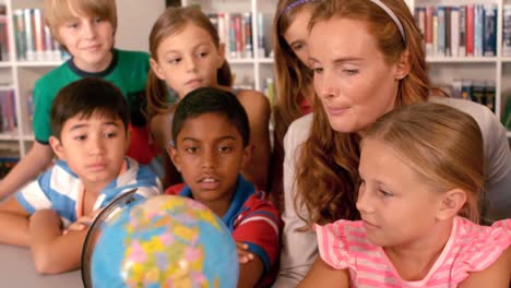 teacher and schoolkids studying globe in library