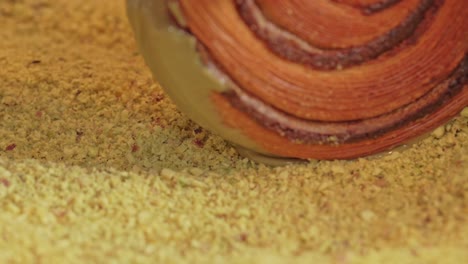 Pistachio croissant donut being rolled over pistachio pieces