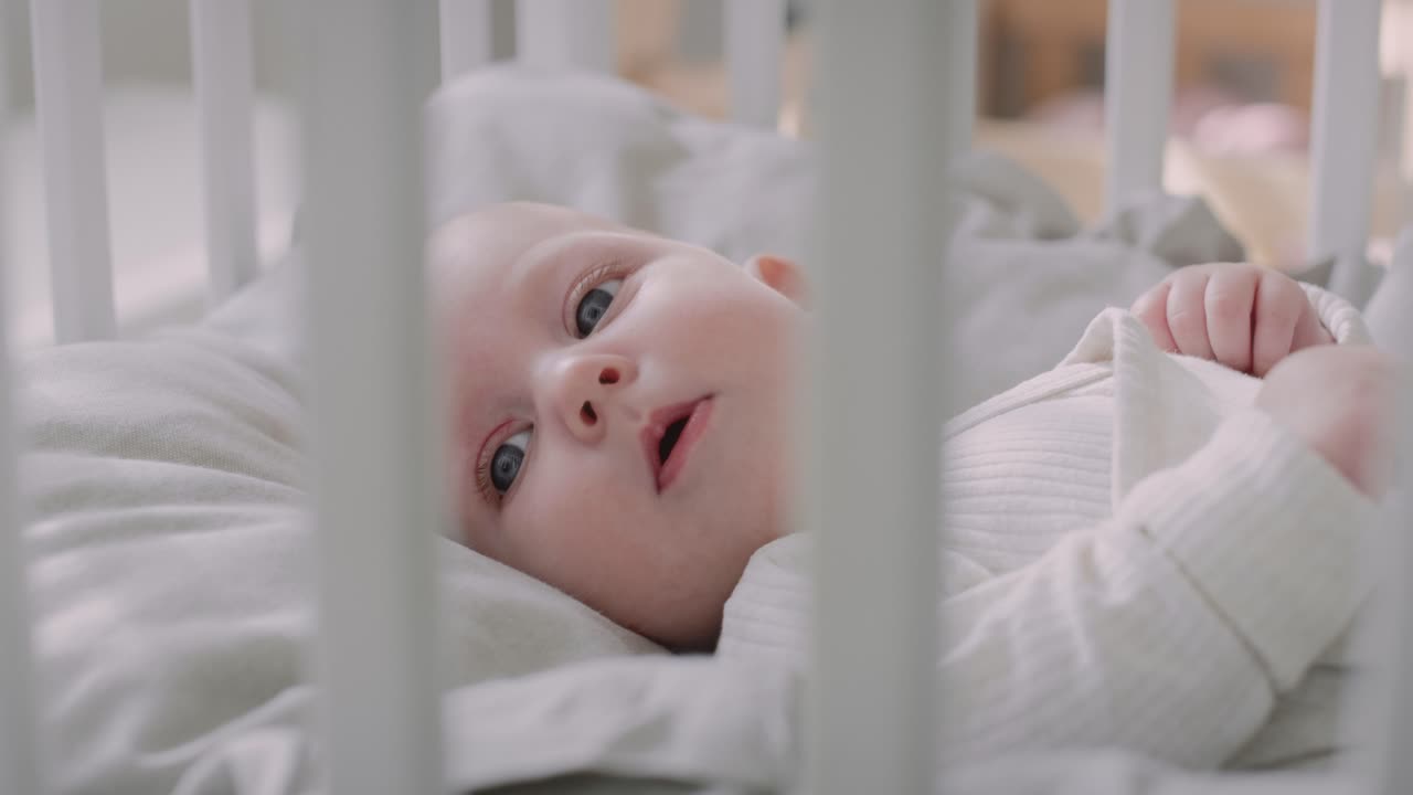 Neonato sdraiato nella culla a pancia in su che guarda la fotocamera.