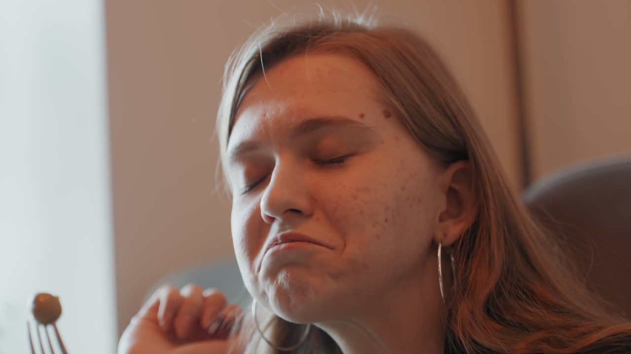 White woman savoring olive on fork in sunlit cafe, closed eyes and gentle smile, freckled skin with hoop earrings, slow appreciative bite, food blogger and home cook roles, intimate closeup, warm